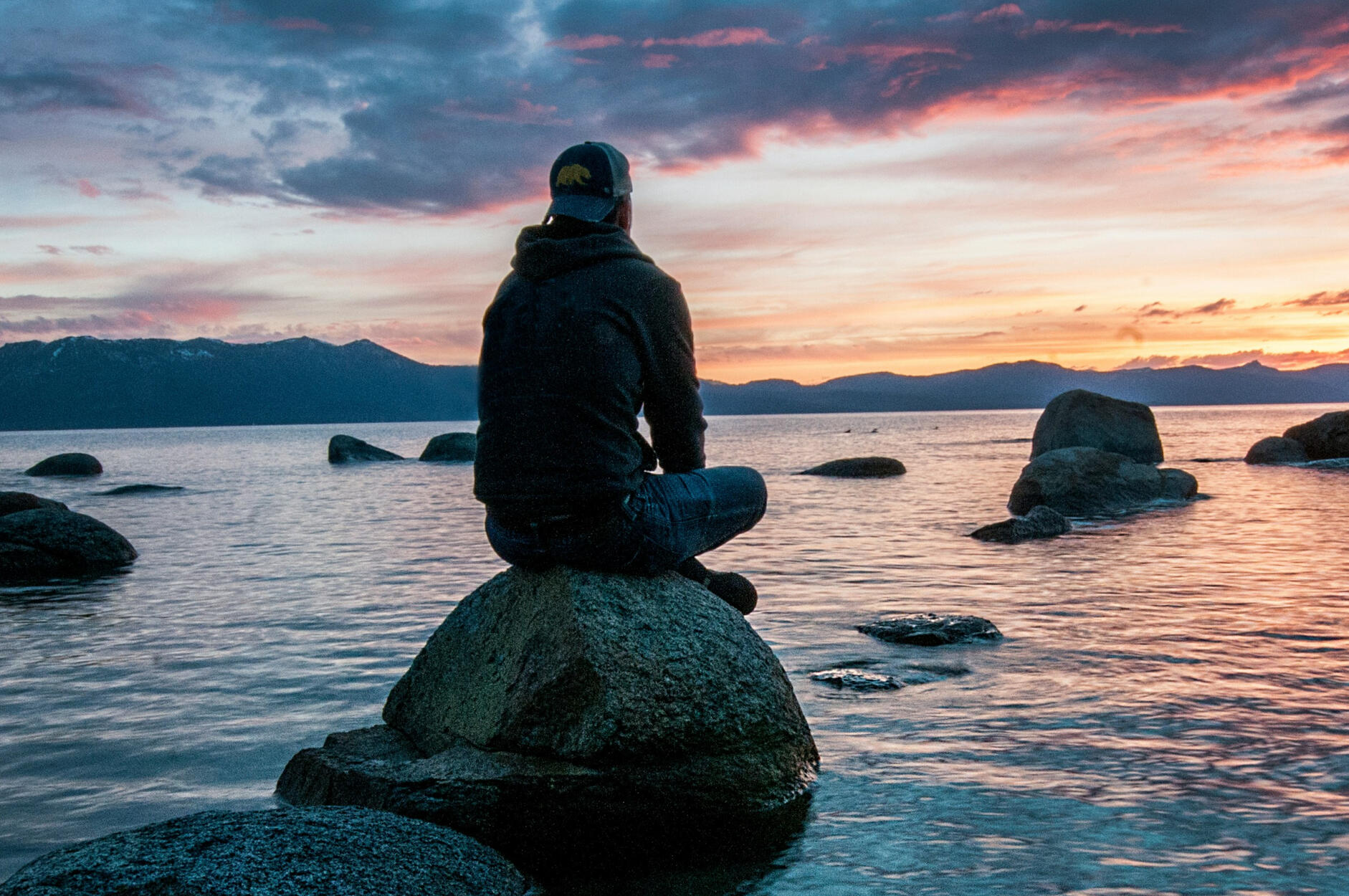 A person sitting on a rock in the ocean watching the sunset