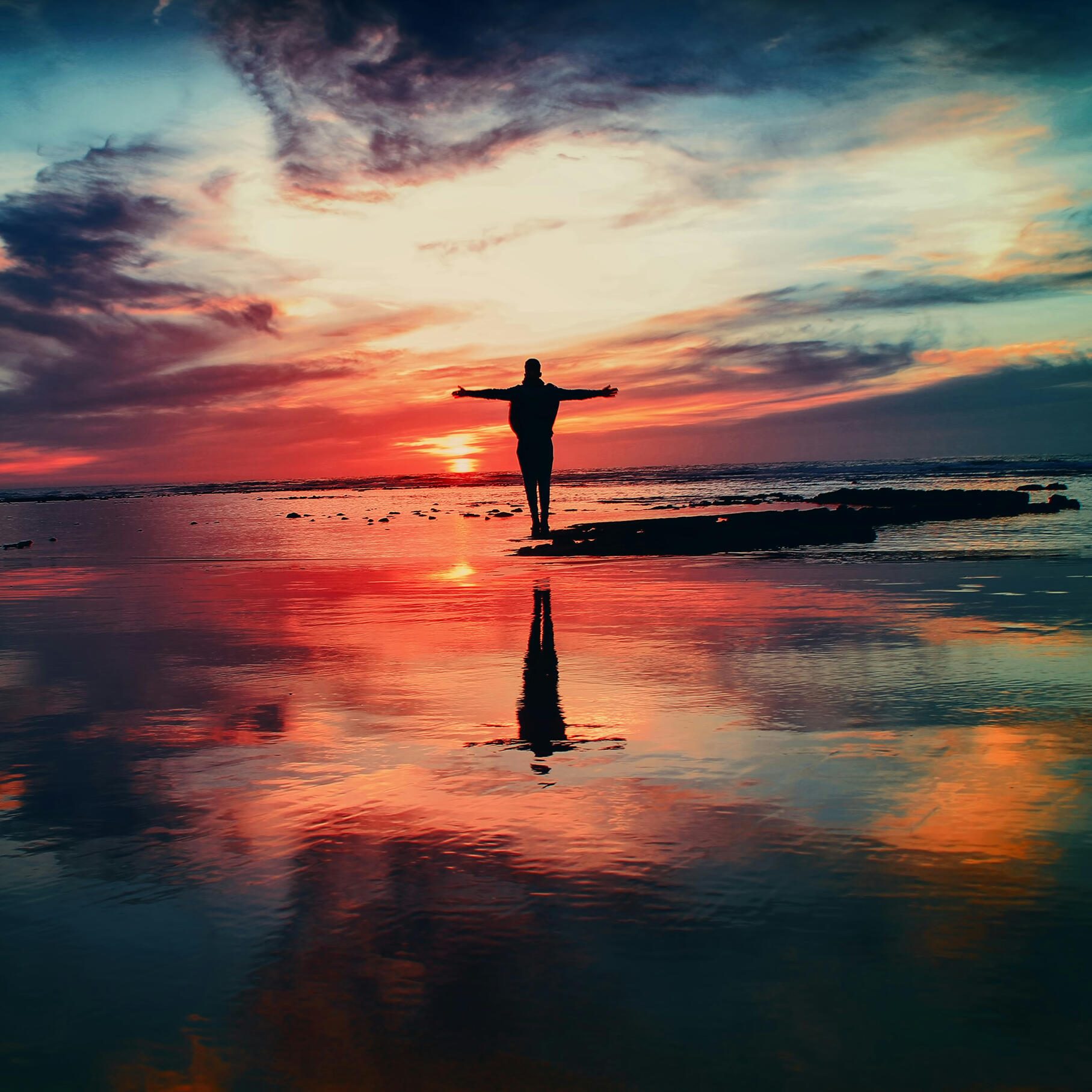 Silhouette of a person standing by the ocean at sunset with arms open